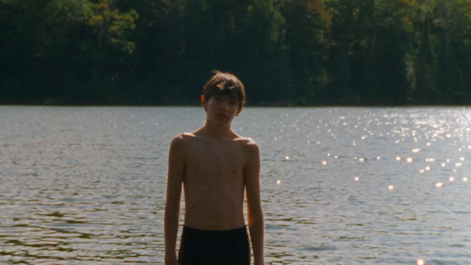 garçon dans un lac avec l'eau jusqu'au genoux, regarde la caméra de face.