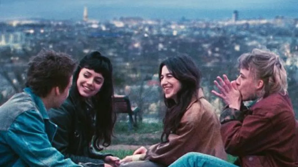 Bildbeschreibung: Ausschnitt des französisches Filmplakats "Les passagers de la nuit". Vier Freunde sitzen auf einer Wiese und lachen. Im Hintergrund ist eine Stadt zu sehen.