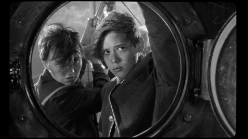 Filmszene aus The wild boys. Zwei Jungen gucken durch ein rundes Fenster.